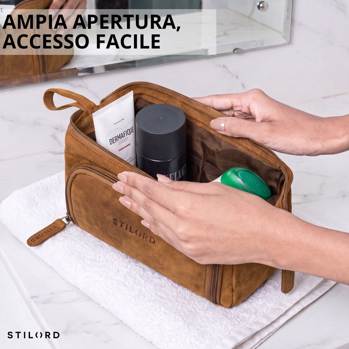 Necessaire in pelle color tan aperto, tasche interne visibili, logo STILORD impresso, mani sul lavabo