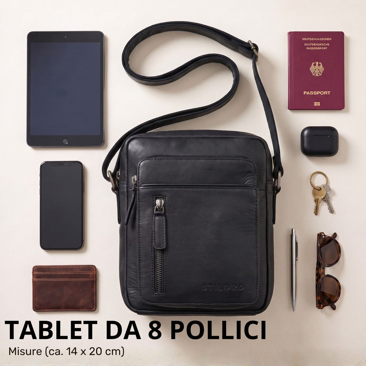 Kleine schwarze Leder-Schultertasche Dain, frontale Ansicht flach liegend, daneben Tablet 8 Zoll, Smartphone, Geldbörse, Reisepass und Zubehör